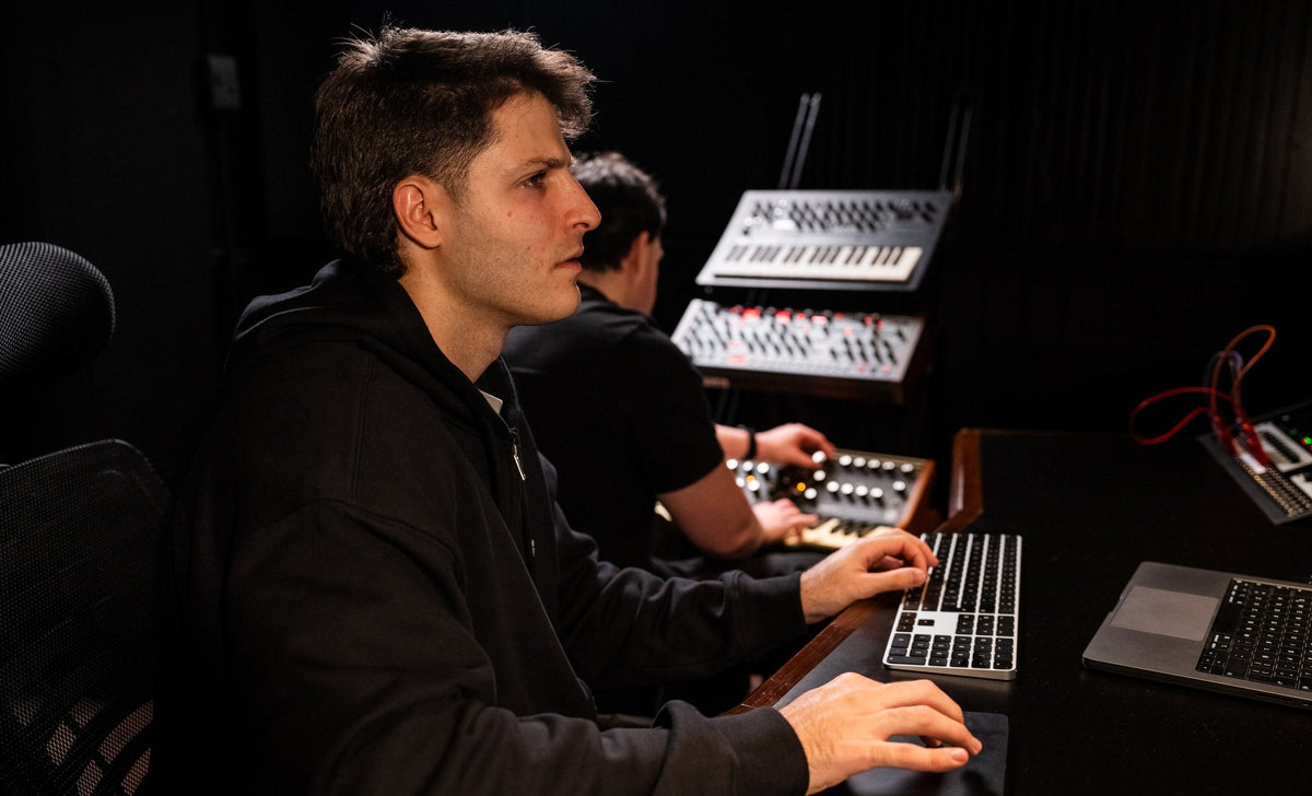 Clase de producción musical en dbel: manos tocando el teclado junto a los sintetizadores